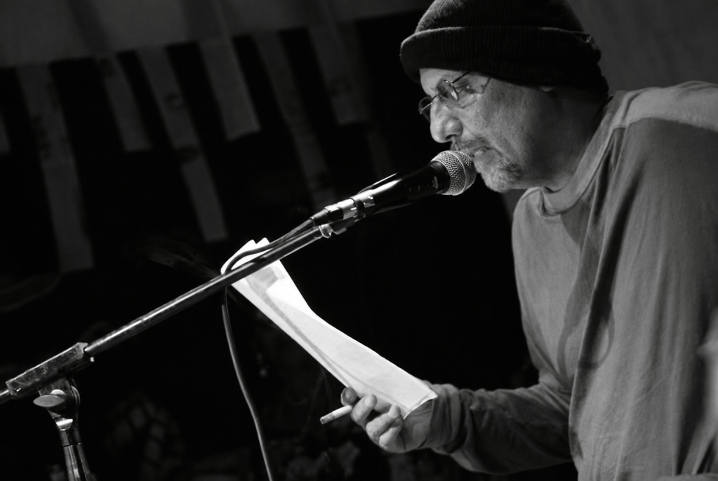 Juan Carlos Flores leyendo ante un micrófono, en blanco y negro.